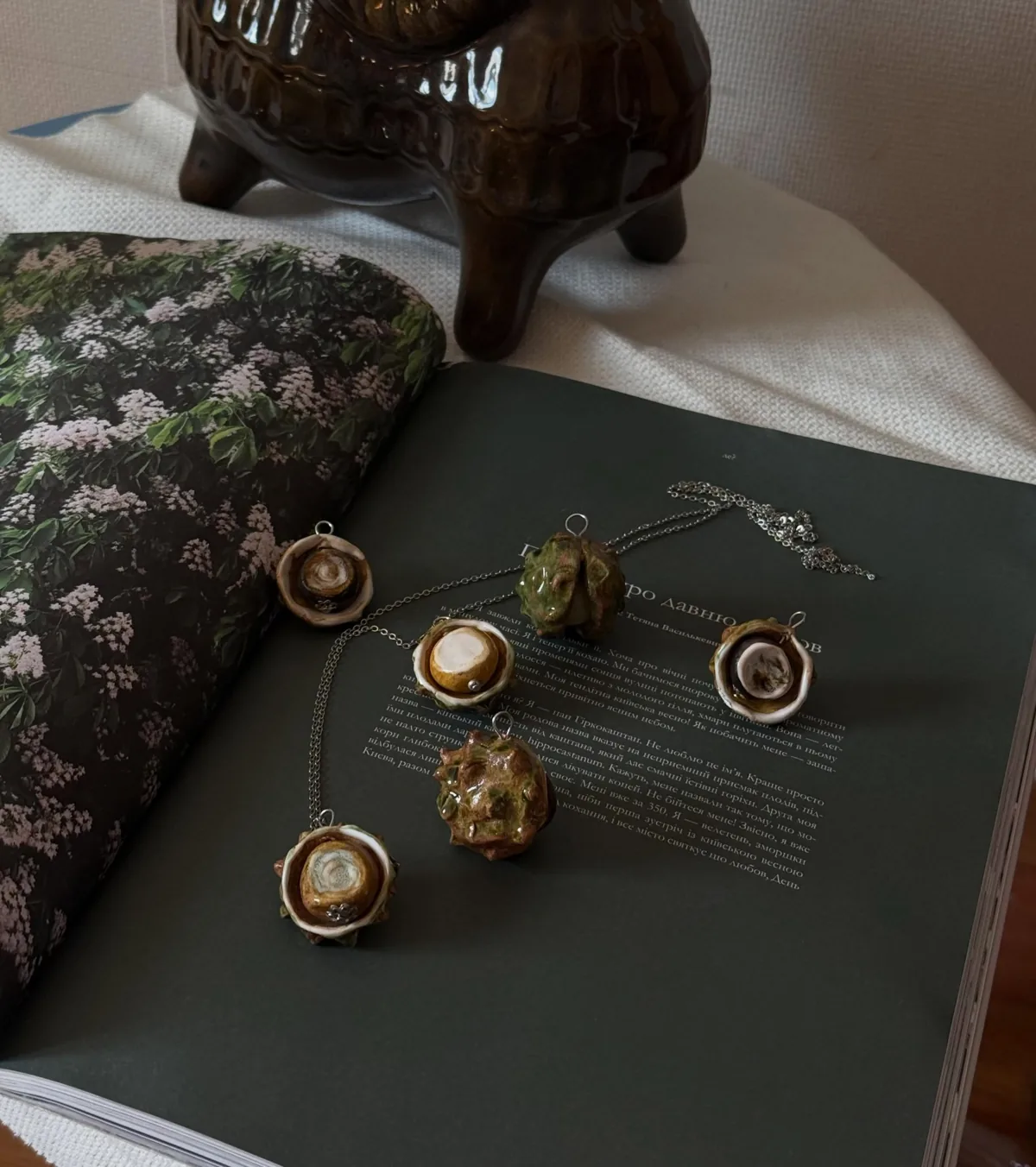 Глазуровані керамічні каштанчики на розгорнутій книжці біля коричневого глечика